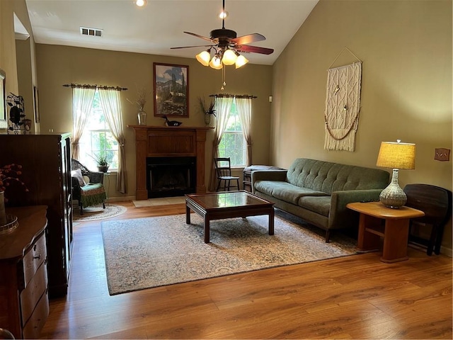 living area with plenty of natural light, a fireplace, light wood-style flooring, a ceiling fan, and vaulted ceiling