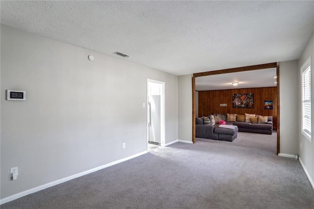 unfurnished living room with baseboards, visible vents, carpet floors, wood walls, and a textured ceiling