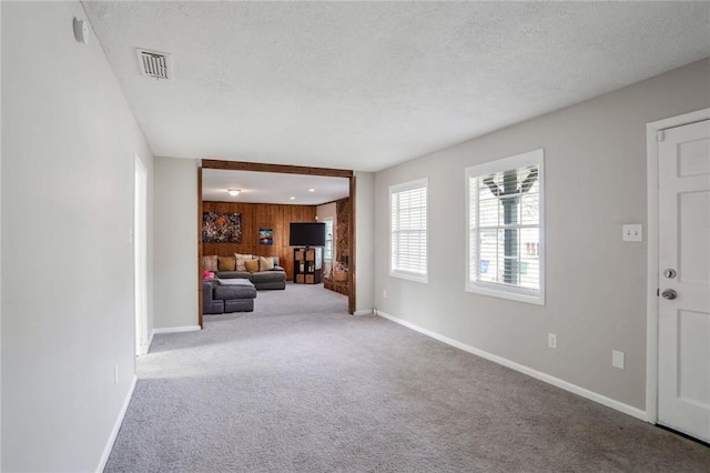 unfurnished living room with visible vents, a textured ceiling, wooden walls, carpet flooring, and baseboards