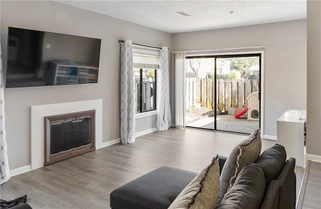 living room with a textured ceiling, a glass covered fireplace, light wood-style flooring, and baseboards