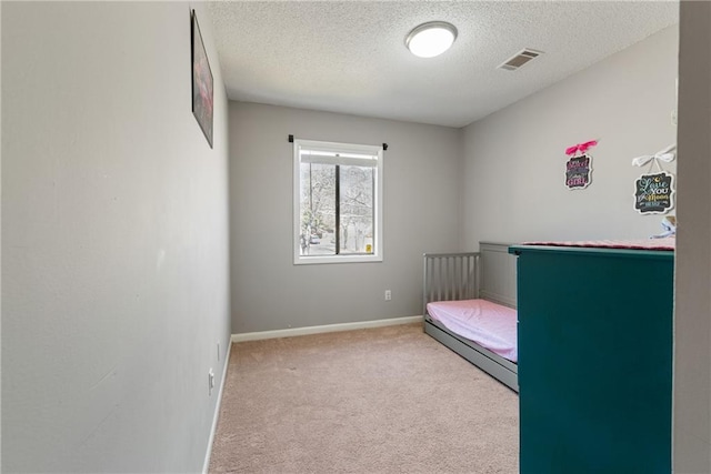 bedroom with a crib, baseboards, visible vents, light colored carpet, and a textured ceiling