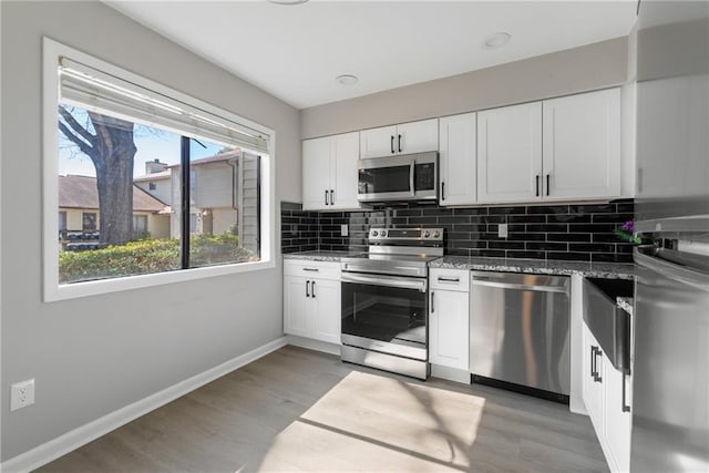 kitchen featuring stainless steel appliances, light stone counters, backsplash, and white cabinets