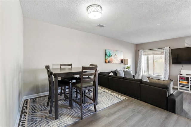 dining space with baseboards, light wood-style flooring, visible vents, and a textured ceiling