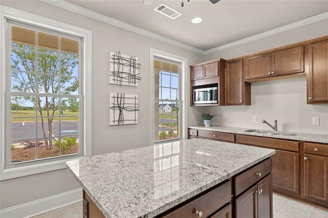 kitchen with a kitchen island, stainless steel microwave, sink, ornamental molding, and light stone counters