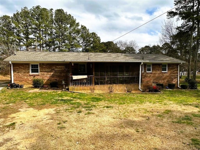 back of property with a sunroom, brick siding, and a yard