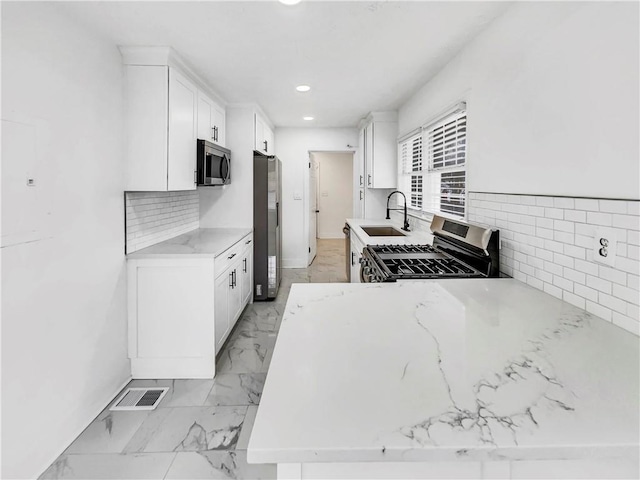 kitchen with sink, light stone counters, appliances with stainless steel finishes, white cabinets, and backsplash