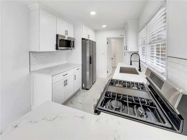 kitchen featuring sink, appliances with stainless steel finishes, light stone counters, white cabinets, and decorative backsplash