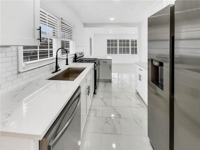 kitchen with light stone counters, stainless steel appliances, sink, and white cabinets