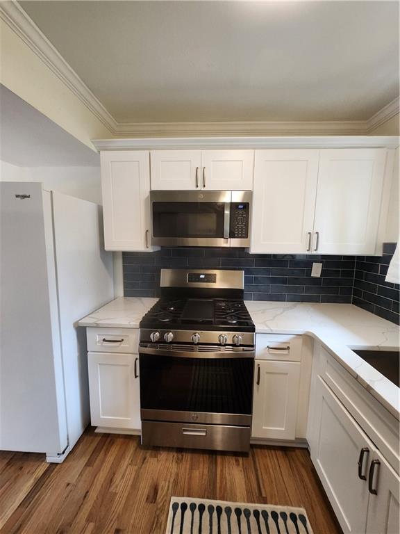 kitchen featuring light stone countertops, stainless steel appliances, white cabinetry, and tasteful backsplash