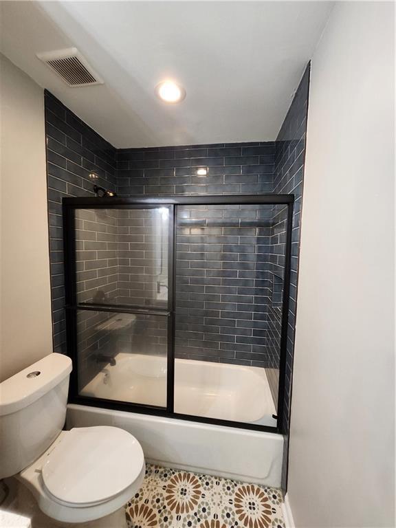 bathroom with bath / shower combo with glass door, tile patterned floors, and toilet