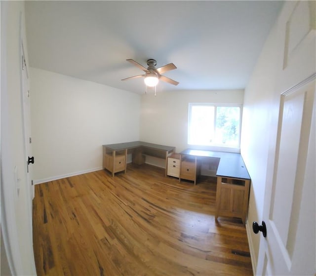 unfurnished office featuring ceiling fan, built in desk, and hardwood / wood-style floors