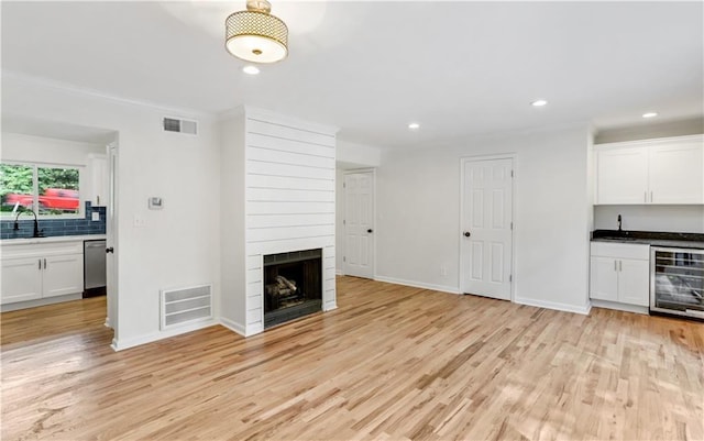 unfurnished living room with sink, a fireplace, light wood-type flooring, and wine cooler