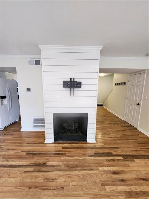 details featuring wood-type flooring, a fireplace, ornamental molding, and white refrigerator with ice dispenser