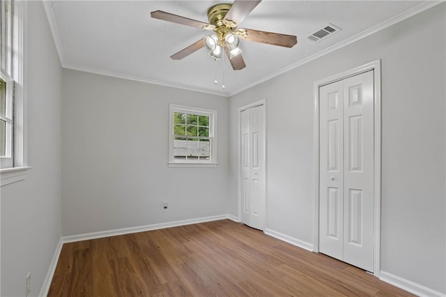 unfurnished bedroom featuring baseboards, multiple closets, visible vents, and wood finished floors