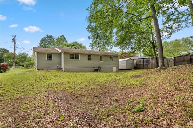 rear view of house featuring fence, a storage shed, crawl space, an outbuilding, and a yard