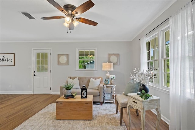living area with visible vents, light wood-style floors, crown molding, and baseboards