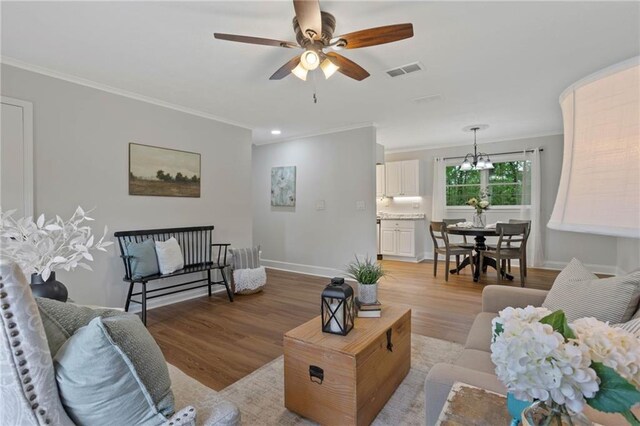 living area featuring crown molding, ceiling fan with notable chandelier, light wood finished floors, and visible vents
