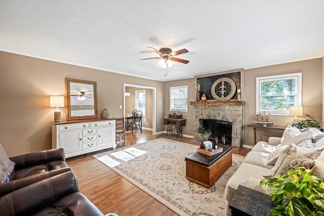 living room with ceiling fan, baseboards, a stone fireplace, and wood finished floors