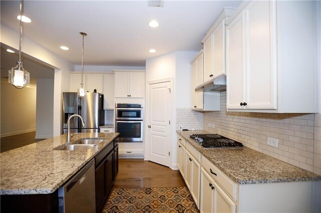 kitchen featuring a kitchen island with sink, white cabinets, sink, appliances with stainless steel finishes, and decorative light fixtures