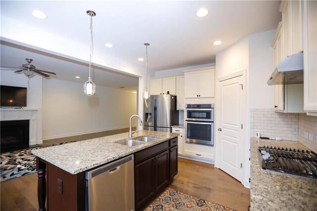 kitchen featuring appliances with stainless steel finishes, dark brown cabinetry, a kitchen island with sink, sink, and hanging light fixtures