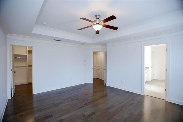 unfurnished bedroom with a walk in closet, dark hardwood / wood-style flooring, ornamental molding, a tray ceiling, and ceiling fan