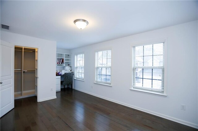 unfurnished bedroom with a closet, built in desk, and dark hardwood / wood-style floors