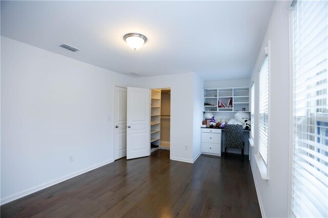 unfurnished bedroom with a walk in closet, a closet, and dark hardwood / wood-style flooring