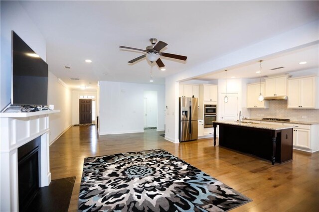 kitchen featuring pendant lighting, dark wood-type flooring, a center island with sink, white cabinets, and appliances with stainless steel finishes