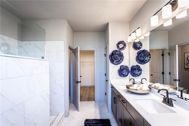 full bath featuring double vanity, marble finish floor, a walk in closet, and a sink