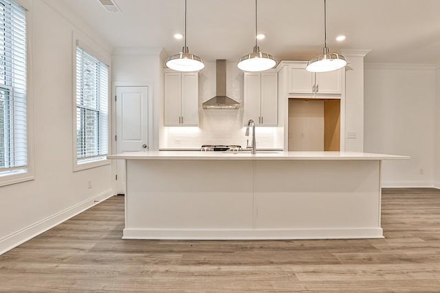 kitchen with decorative light fixtures, a kitchen island with sink, and wall chimney exhaust hood