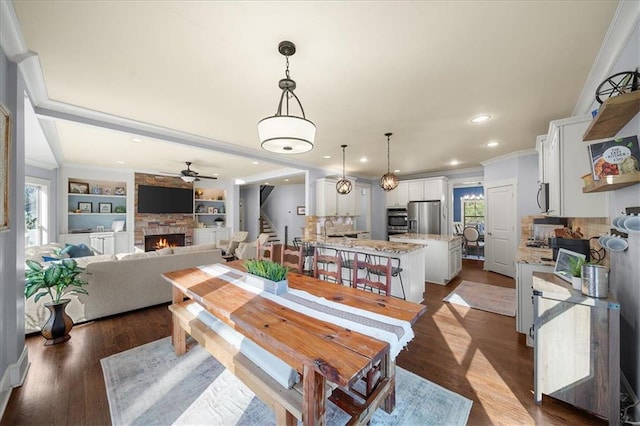 dining space with a fireplace, a healthy amount of sunlight, built in features, and ornamental molding