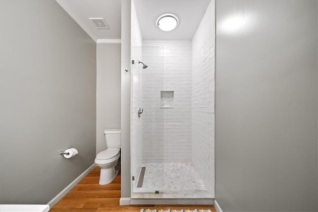 bathroom with tiled shower, hardwood / wood-style floors, ornamental molding, and toilet