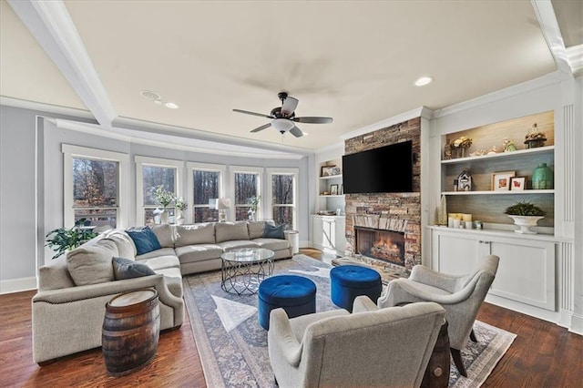 living room with ceiling fan, built in features, dark hardwood / wood-style floors, crown molding, and a fireplace