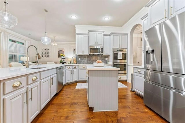 kitchen with decorative light fixtures, light countertops, backsplash, appliances with stainless steel finishes, and a sink