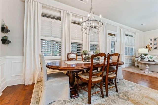 dining area featuring a wainscoted wall, a decorative wall, a notable chandelier, and wood finished floors