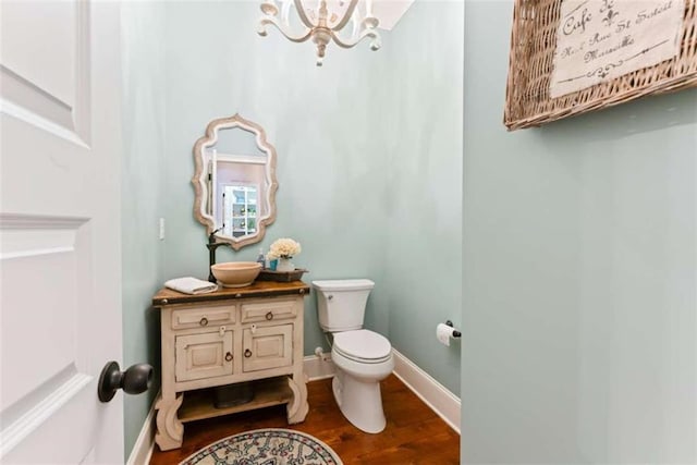 half bath featuring toilet, wood finished floors, vanity, baseboards, and an inviting chandelier