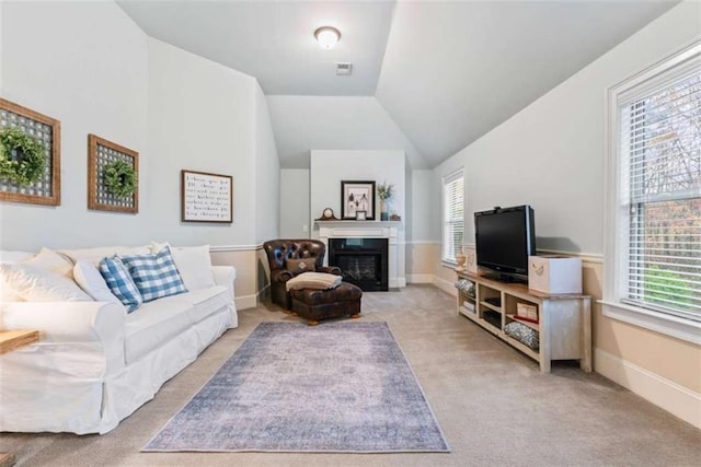 living area with visible vents, a glass covered fireplace, light carpet, vaulted ceiling, and baseboards