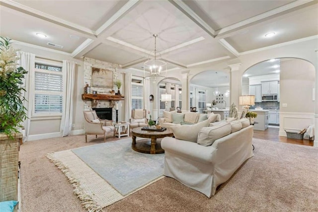 living room with coffered ceiling, a notable chandelier, a stone fireplace, and beamed ceiling