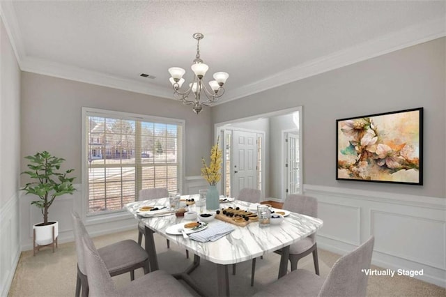 dining area with visible vents, light colored carpet, ornamental molding, a chandelier, and a decorative wall