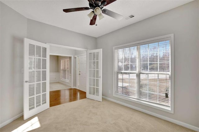 carpeted empty room with visible vents, ceiling fan, a wealth of natural light, and baseboards