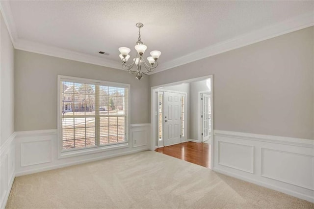 carpeted empty room with crown molding, visible vents, a decorative wall, an inviting chandelier, and a textured ceiling