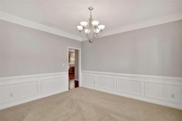 empty room with light carpet, an inviting chandelier, crown molding, and a wainscoted wall