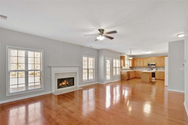 unfurnished living room with light wood-style floors, baseboards, a ceiling fan, and a glass covered fireplace