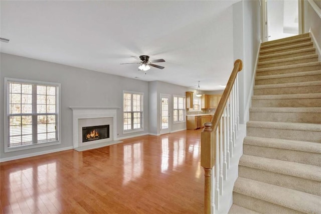 unfurnished living room with baseboards, a ceiling fan, a fireplace with flush hearth, stairway, and wood finished floors