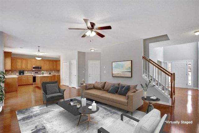 living area featuring a ceiling fan, light wood-type flooring, baseboards, and stairs