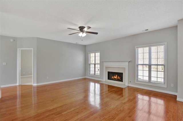 unfurnished living room featuring wood finished floors, a ceiling fan, visible vents, baseboards, and a glass covered fireplace