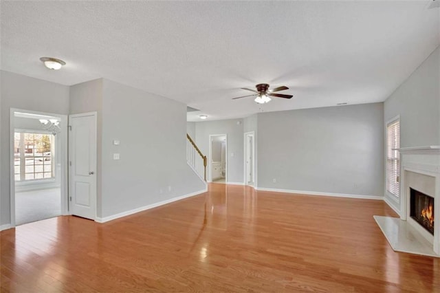 unfurnished living room featuring a glass covered fireplace, stairway, baseboards, and wood finished floors