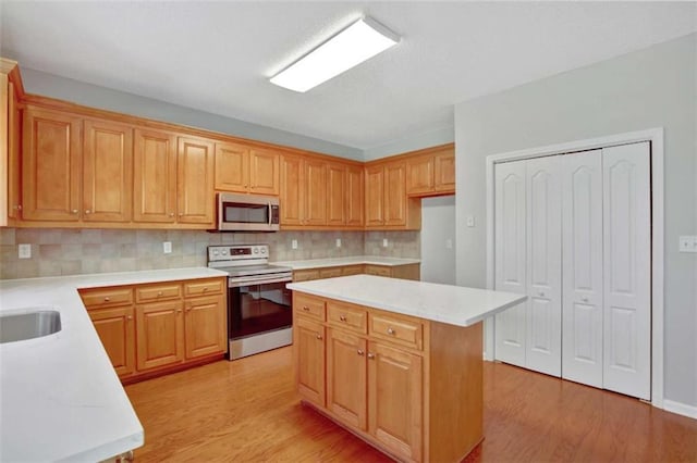 kitchen featuring light wood-style flooring, stainless steel microwave, light countertops, backsplash, and range with electric stovetop