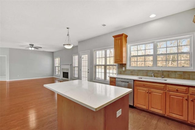 kitchen featuring a fireplace, light countertops, decorative backsplash, a sink, and dishwasher