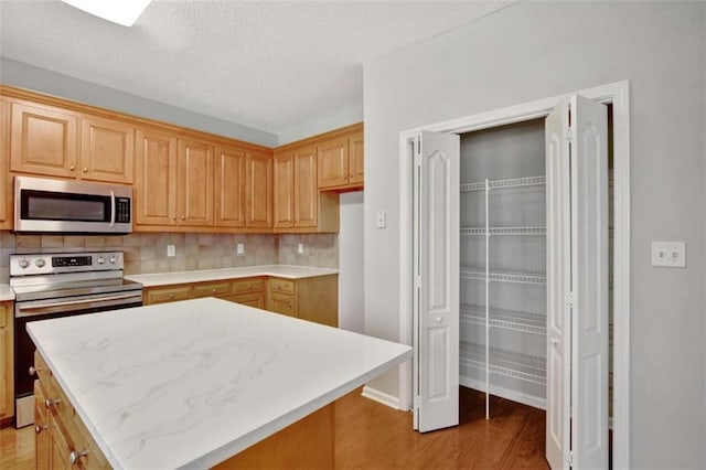 kitchen featuring tasteful backsplash, appliances with stainless steel finishes, a textured ceiling, light brown cabinetry, and light wood-type flooring